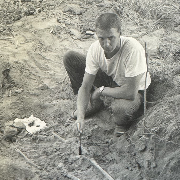 Man carefully excavating an object in the sand.