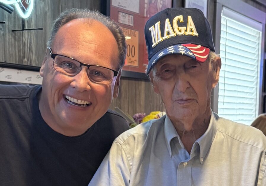 Two men smiling, one wearing a MAGA hat.
