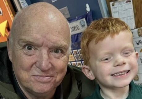 Smiling older man with a young red-haired child indoors.